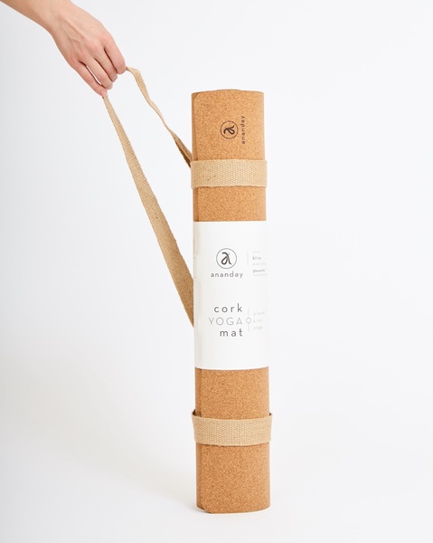 A clean, high-contrast studio shot of a branded cork yoga mat held by a hand, emphasizing the product's natural texture and brand identity.